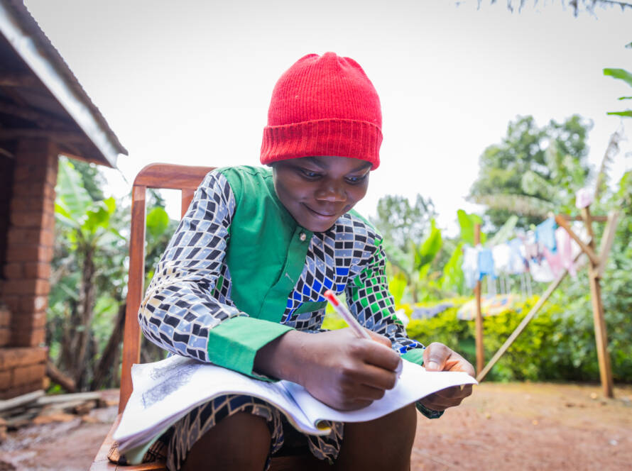 Young school boy sitting outside his home in the village doing his homework.