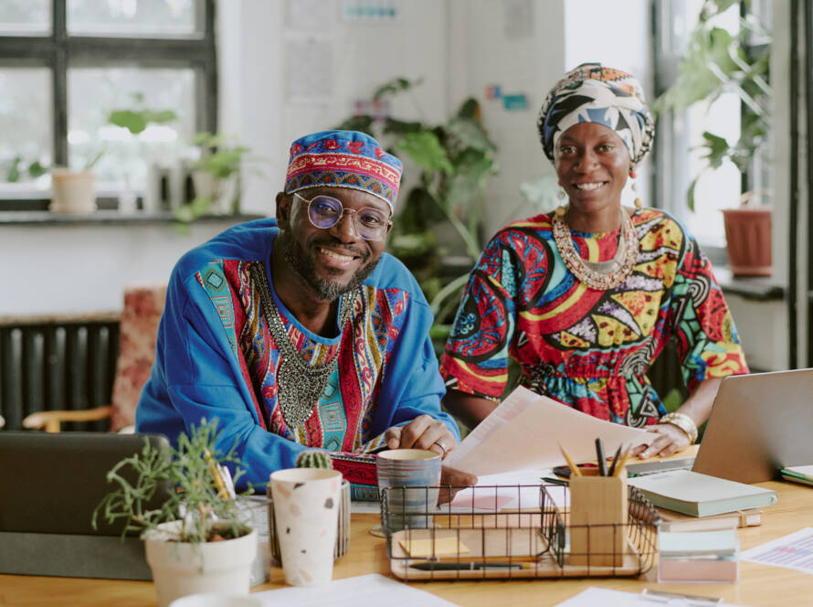 Portrait of smiling African American coworker sitting at wooden table with laptops and documents
